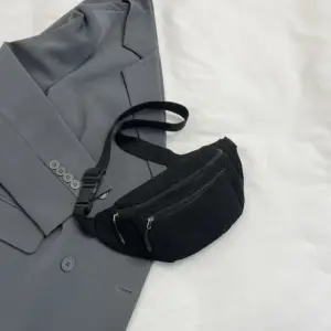 Schwarze Cord-Bauchtasche mit zwei Reißverschlüssen, flach auf einem grauen Blazer