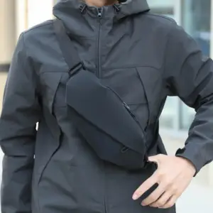 Schwarze kantige Umhängetasche, schräg über der grauen Jacke getragen