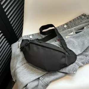 Schwarze Nylon-Bauchtasche mit Reißverschluss, flach auf einer Jeansjacke liegend
