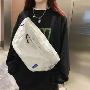 Weiße Bauchtasche mit Karomuster wird vor dem Körper getragen, schwarzer Pullover