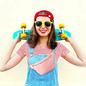 Rosa Bauchtasche, von einer lachenden Frau mit Skateboard und Latzhose getragen