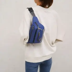 Blaue Bauchtasche mit mehreren Reißverschlussfächern, über der Schulter einer Frau getragen