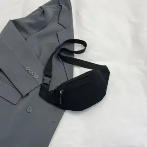 Schwarze Bauchtasche aus Cord liegt auf einem grauen Blazer, Gurt mit Steckschnalle