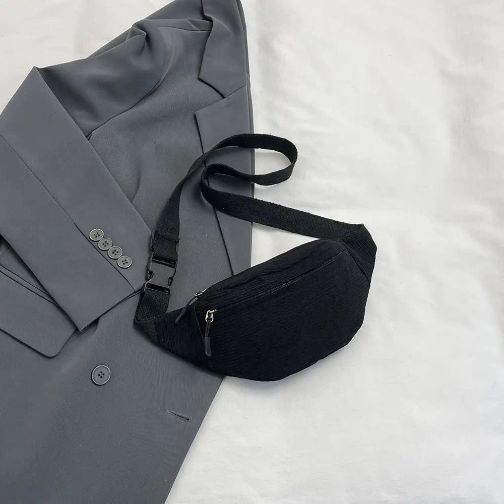 Schwarze Bauchtasche aus Cord auf einem grauen Blazer, Gurt mit Steckschnalle