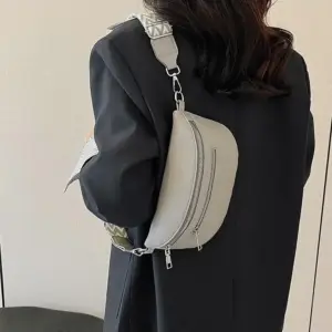 Hellgraue Umhängetasche mit Reißverschlüssen und gemustertem Gurt, an einer Frau im Blazer