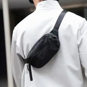 Person trägt eine blaue Bauchtasche aus Stoff über der Schulter vor grauem Pullover