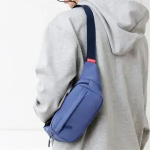 Person trägt eine kleine schwarze Gürteltasche über der Schulter, Rückansicht, vor hellem Hintergrund