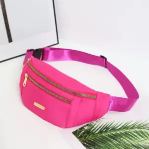 Pinke Bauchtasche aus Nylon mit zwei goldenen Reißverschlüssen, schräg von vorn auf weißem Untergrund
